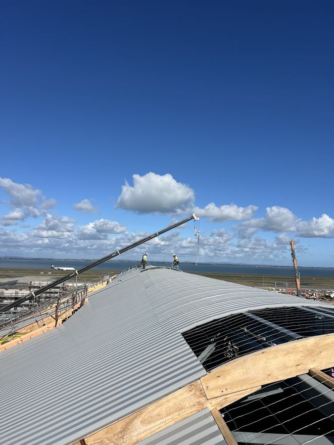 Project Unite roofers on the curved standing seam roof of the domestic processor, with a crane and the runway behind